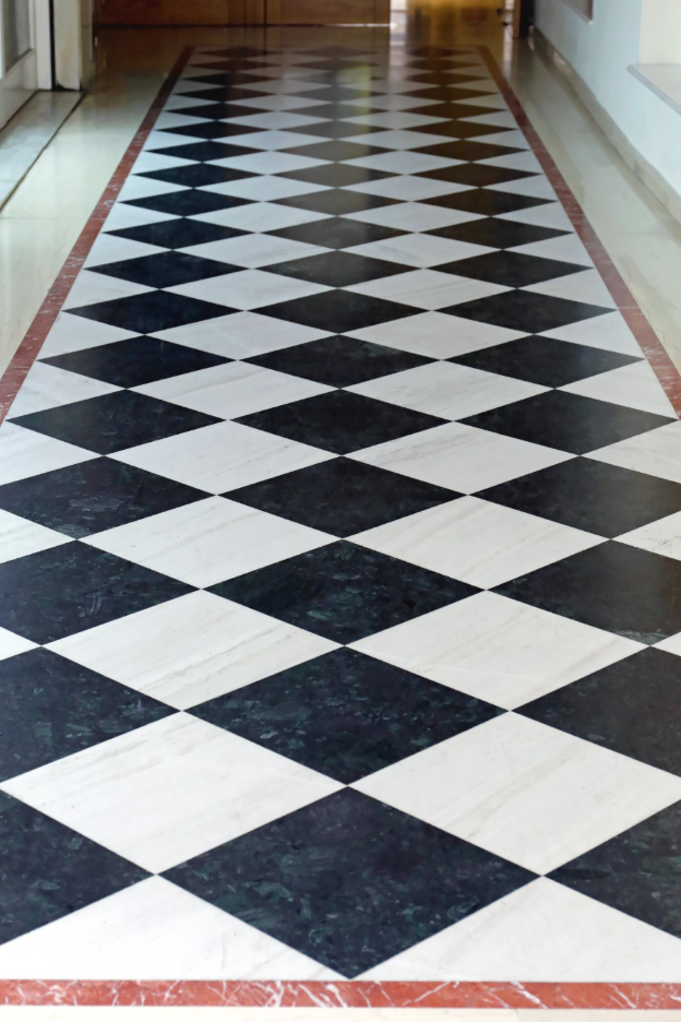 Neo Deco black-and-white geometric tile flooring in a diamond pattern, framed by a contrasting red marble border in a hallway